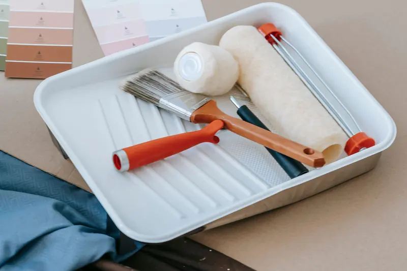 Un bac à peinture avec un rouleau et deux pinceaux.