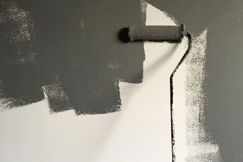 Un rouleau chargé de peinture grise sur un mur partiellement peint.